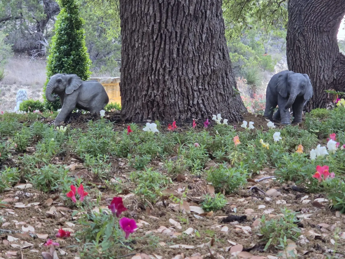 Two elephant statues beneath tree among flowers